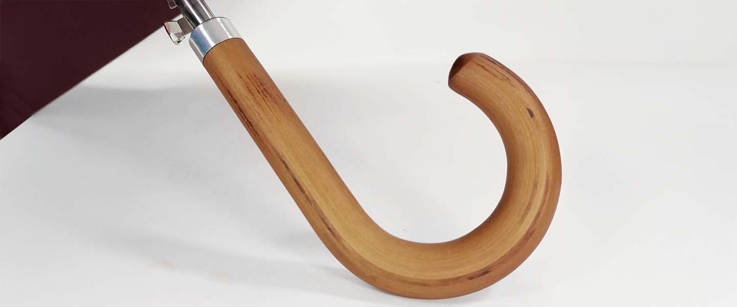 Dettaglio del manico curvo in legno di un ombrello, con finitura liscia e dettagli in metallo.